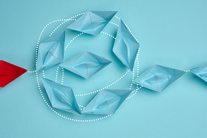 A red paper boat leads blue boats connected by dotted lines, a Business Photo by ndanko