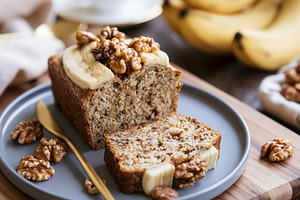 Banana bread loaf with a slice cut, topped with walnuts and banana. Perfect swe, a Photo by Studio ANNA
