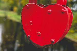 A red heart-shaped padlock attached to a metal railing with a blurred natural b, an Industrial Photo by Textures & Backgrounds