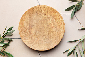 Empty round wooden plate with olive branches on tiled surface, a Background Photo by Olena Rudo