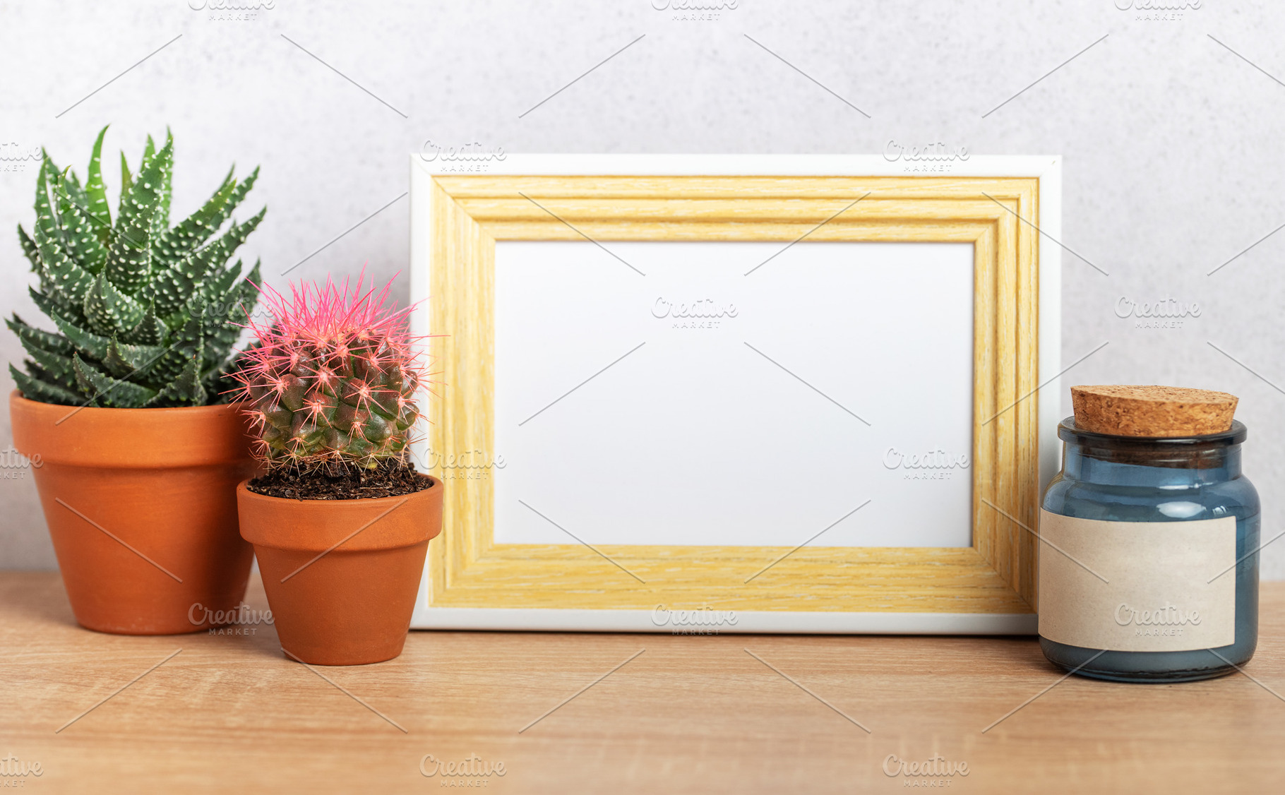 Empty frame mockup with cacti and blue jar on wooden table, a Background Photo by Olena Rudo