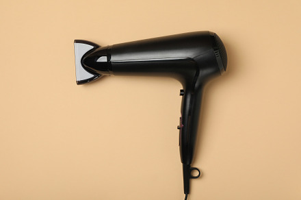 Black hair dryer on beige background, space for text, a Beauty & Fashion Photo by AtlasStudio PRO
