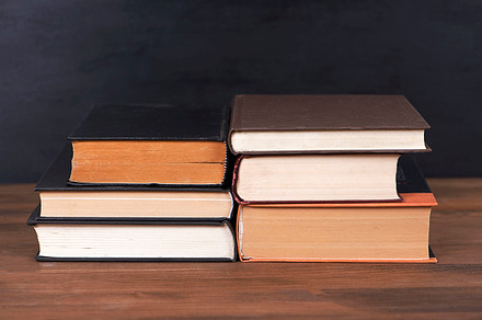 Books stacked on brown wooden table and black background., a School & Education Photo by José Luis Agudo