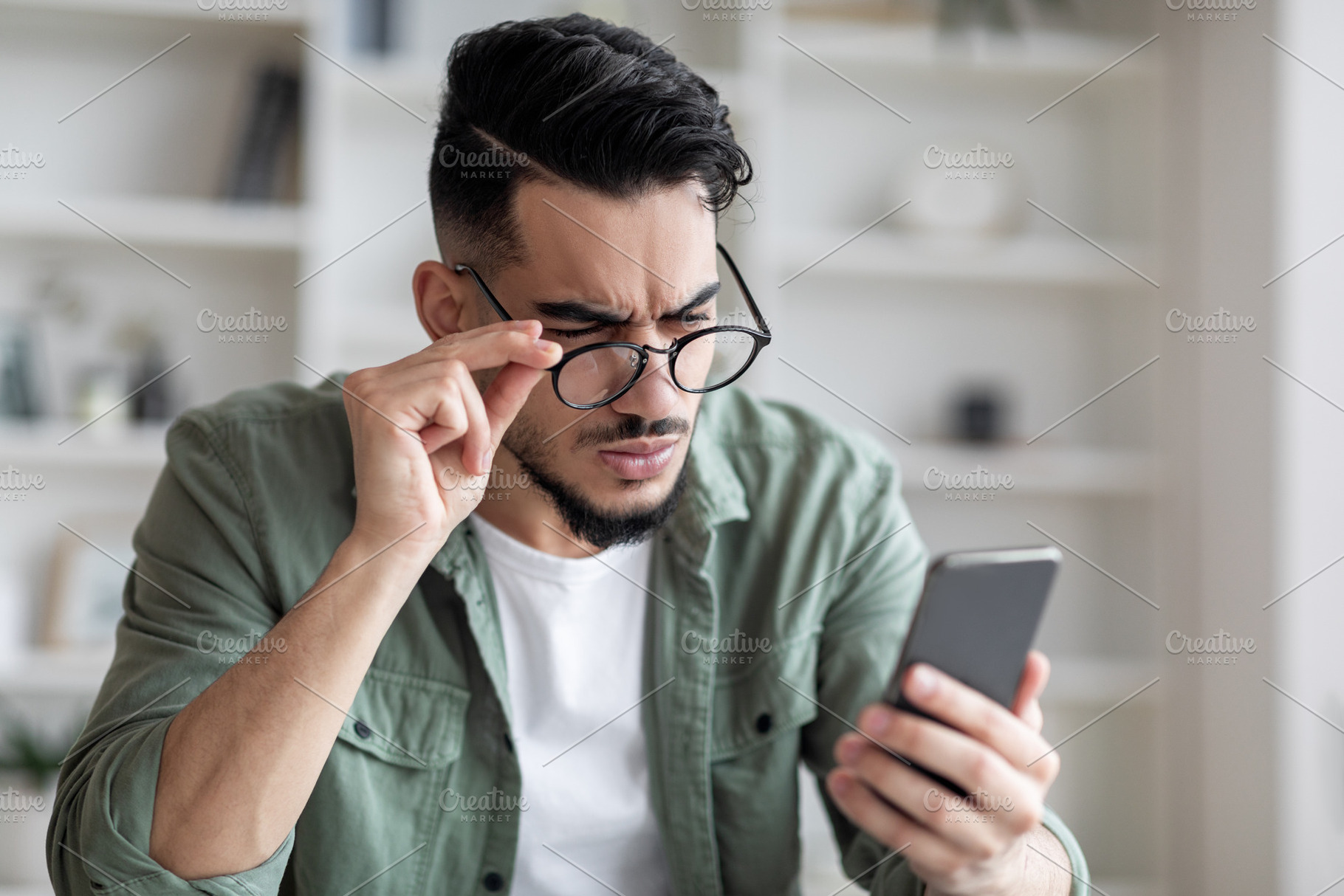 Eyesight Problems Concept. Young Arab Man In Eyeglasses Looking At Smartphone S, a Photo by Prostock-Studio