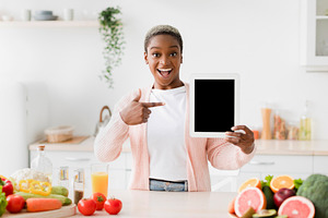 Glad excited emotional young pretty black woman points finger at tablet with bl, a Person Photo by Prostock-Studio