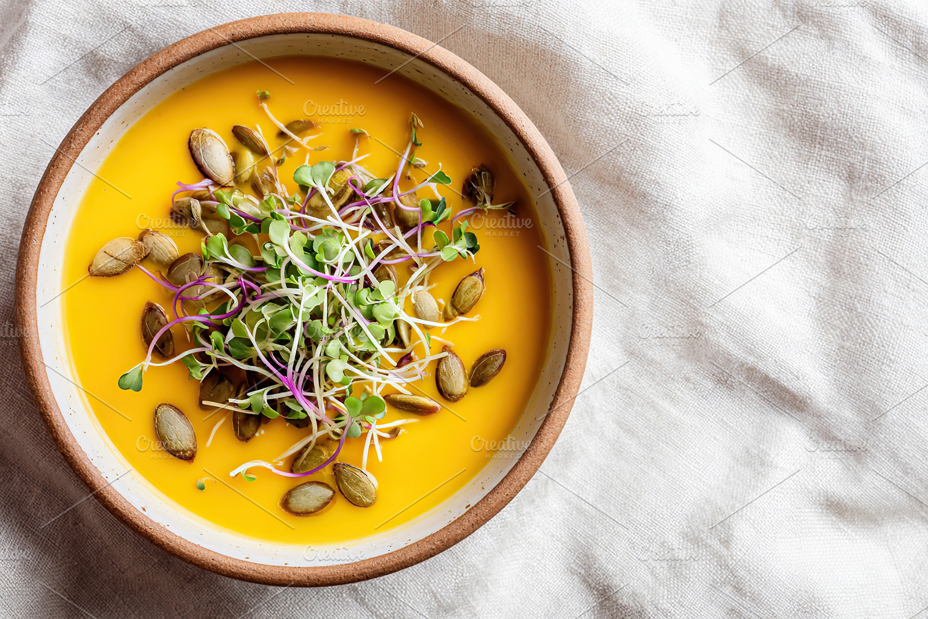 A bowl of rich pumpkin soup placed on a linen napkin, topped with seeds and fre, a Food & Drink Photo by AlyaAnd