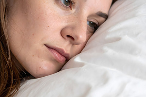 Young woman resting sideways on pillow with thoughtful look, a Person Photo by GoodGoods