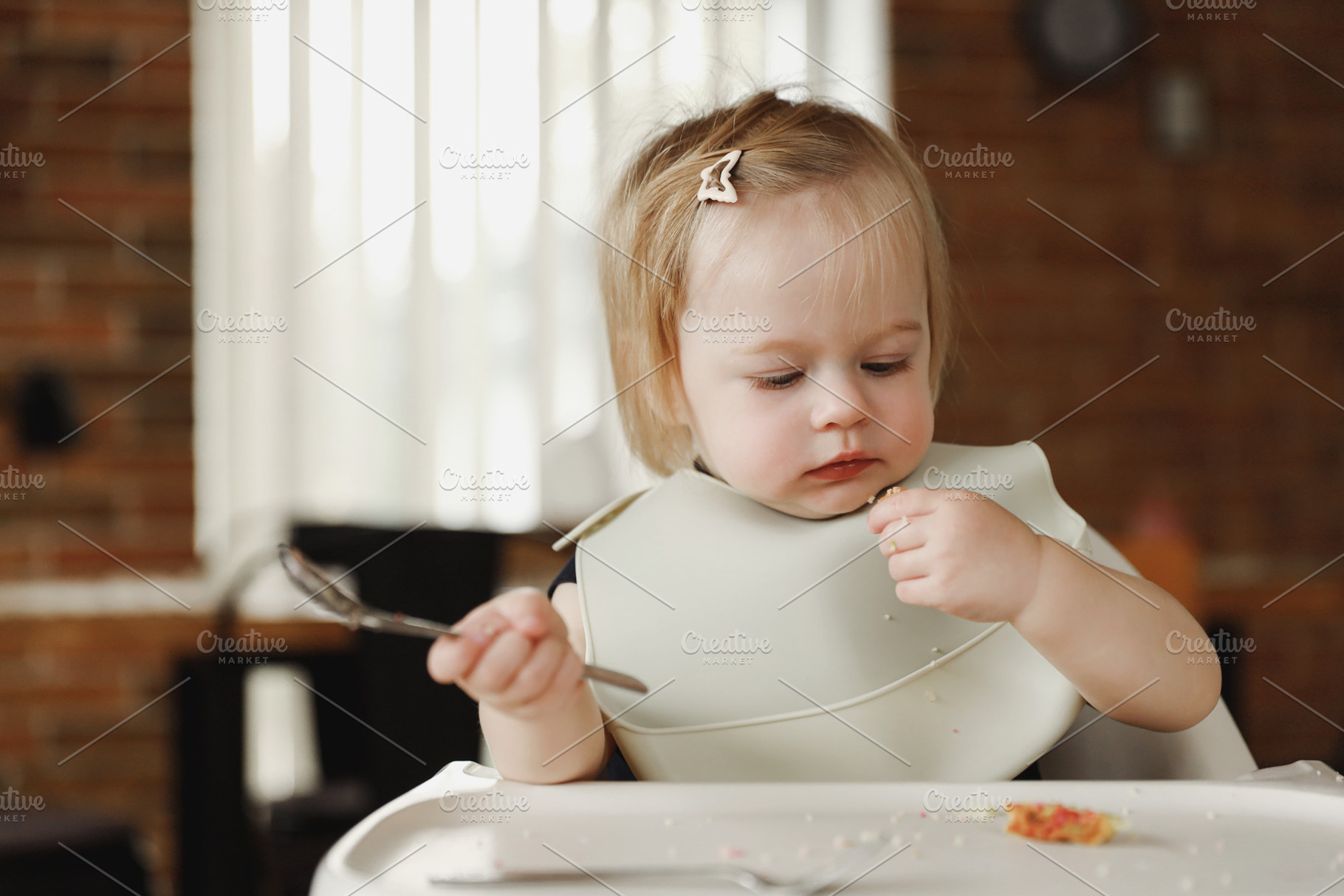 Infant girl or toddler sitting on high chair. Eating food by herself using spoo, a Person Photo by Lenor4ik
