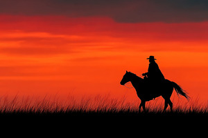 Cowboy on horseback silhouetted against vivid red and orange sun, a Person Photo by José Manuel Gelpi