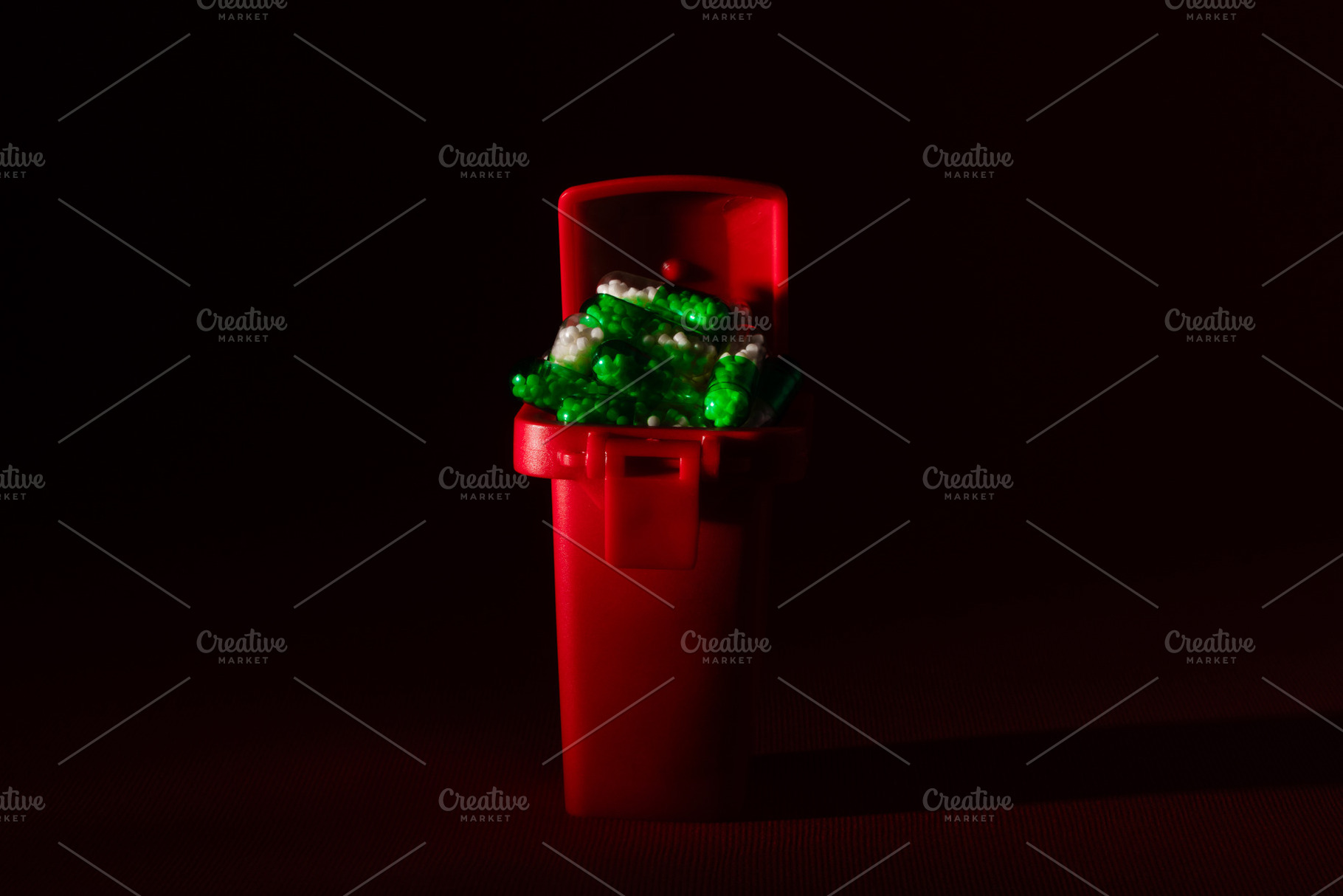 Small red trash bin filled with green and white plastic pieces, isolated on a d, a Health & Medical Photo by Ales Munt