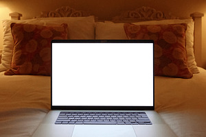 Laptop with blank white screen on a bed, lit by lamps, representing remote work, a Photo by Studio ANNA