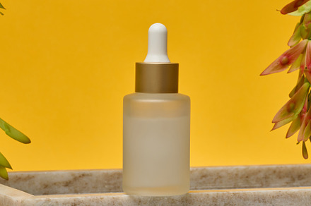 Glass frosted bottle with white pipette on marble stand, cosmeti