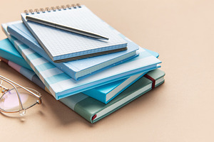 Stack of blue notebooks with pen and glasses