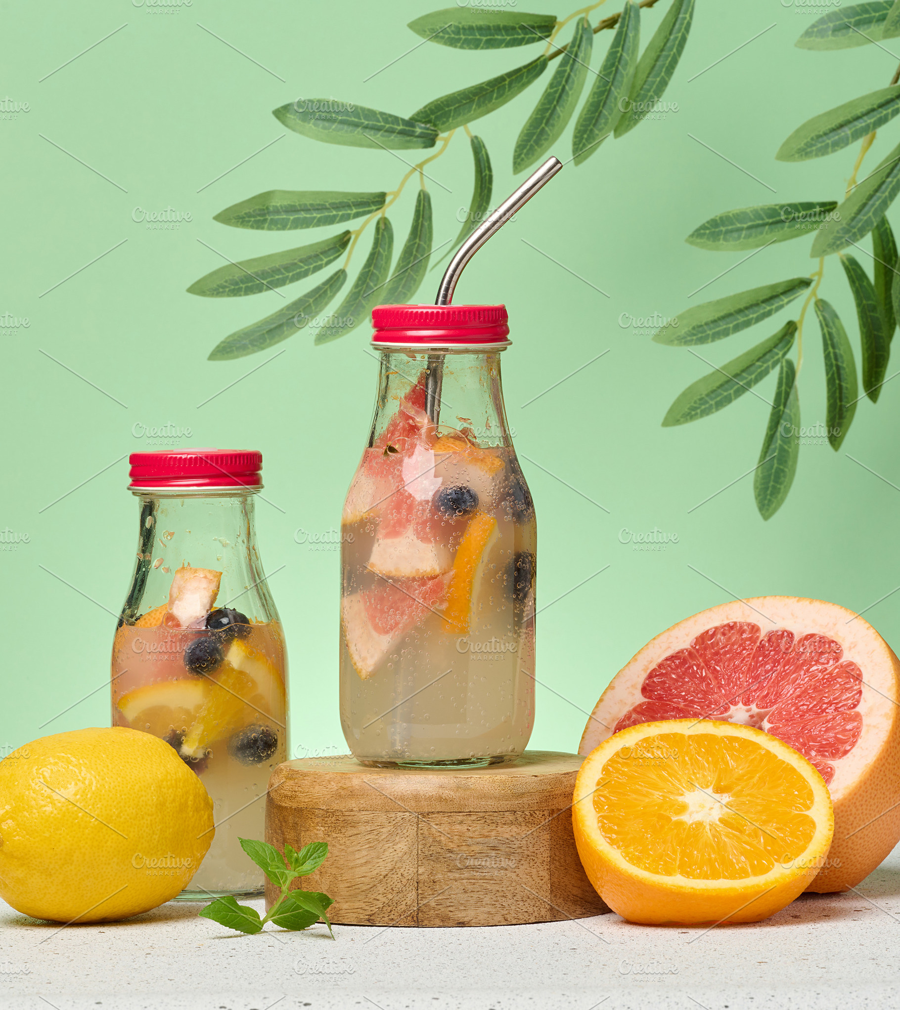 Glass bottles with lemonade and citrus fruit pieces on green bac, a Food & Drink Photo by ndanko