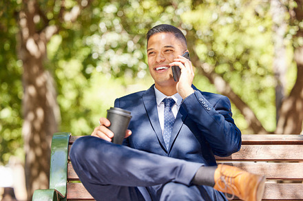 Businessman, phone call and coffee talking on bench outdoor in morning for online conversation, virtual meeting or relax happy on corporate break. Man, sitting on bench and speaking on mobile in park, a Photo by Peopleimages.com