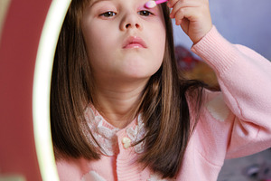 Little girl pretending to apply eye shadow looking in a toy vanity mirror., a Person Photo by Rohan Photography