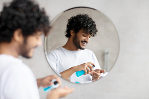Young indian man applying shaving foam standing in modern bathroom and preparin, a Person Photo by Prostock-Studio