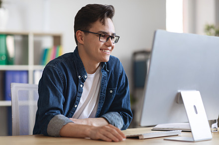 Portrait Of Smiling Millennial Businessman Working On Computer In Office, a Photo by Prostock-Studio
