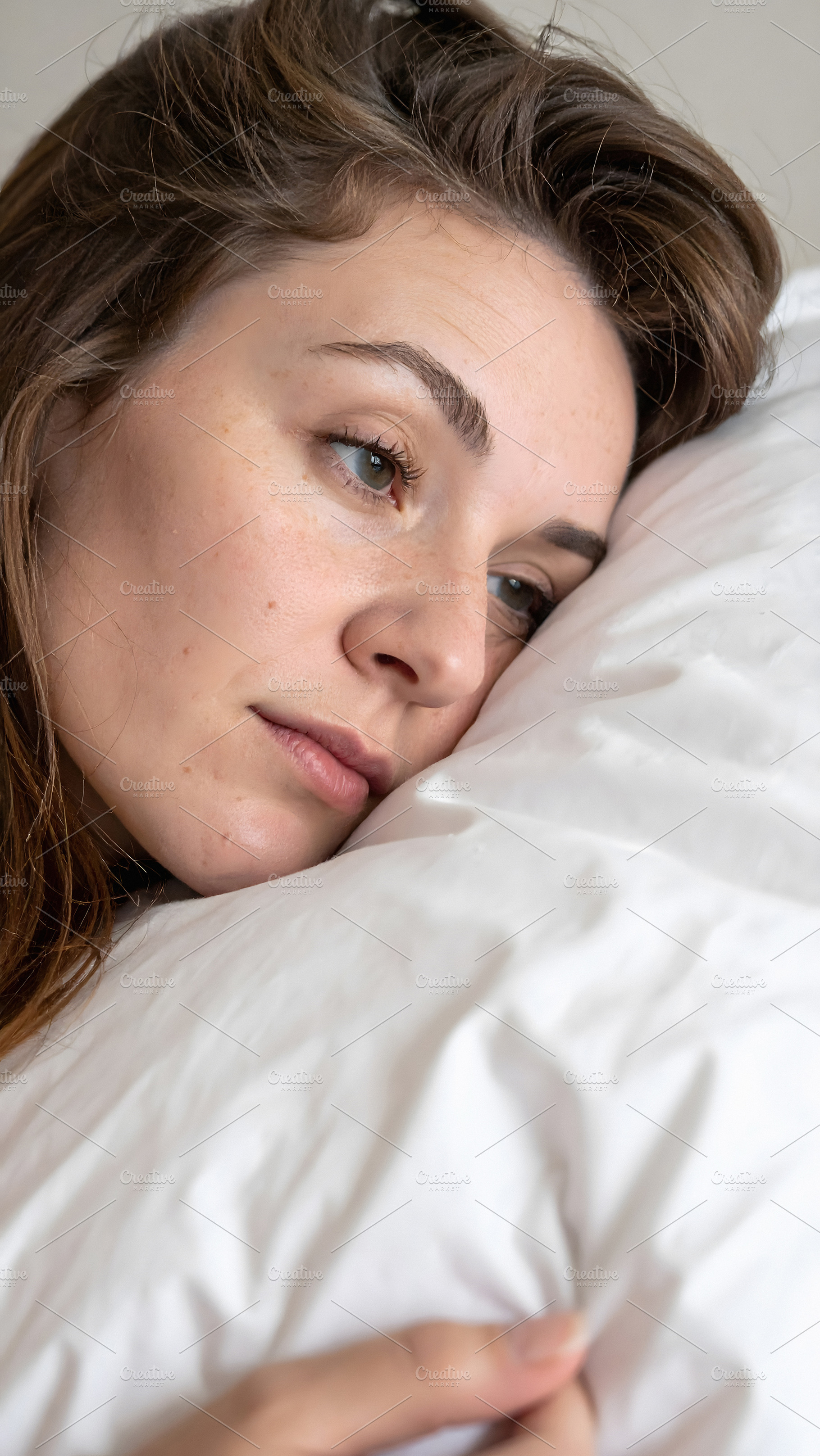Young woman resting sideways on pillow with thoughtful look, a Person Photo by GoodGoods