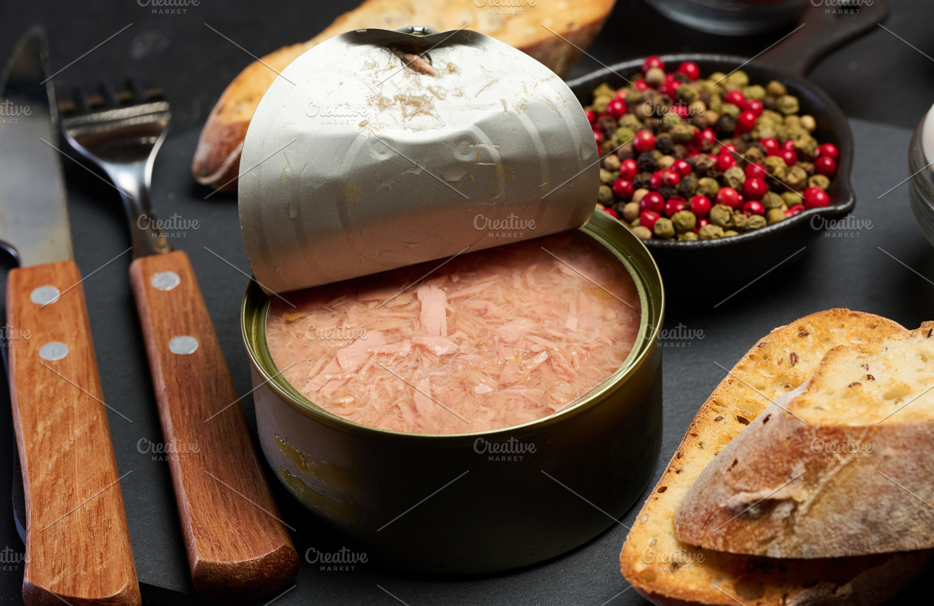 A can of tuna and toasted baguette slices on a black table, a Food & Drink Photo by ndanko