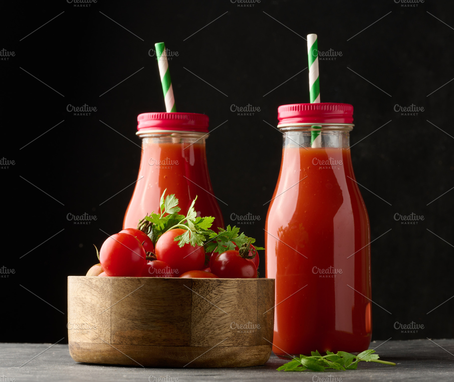 Glass bottles with tomato juice on black table and wooden bowl w, a Food & Drink Photo by ndanko