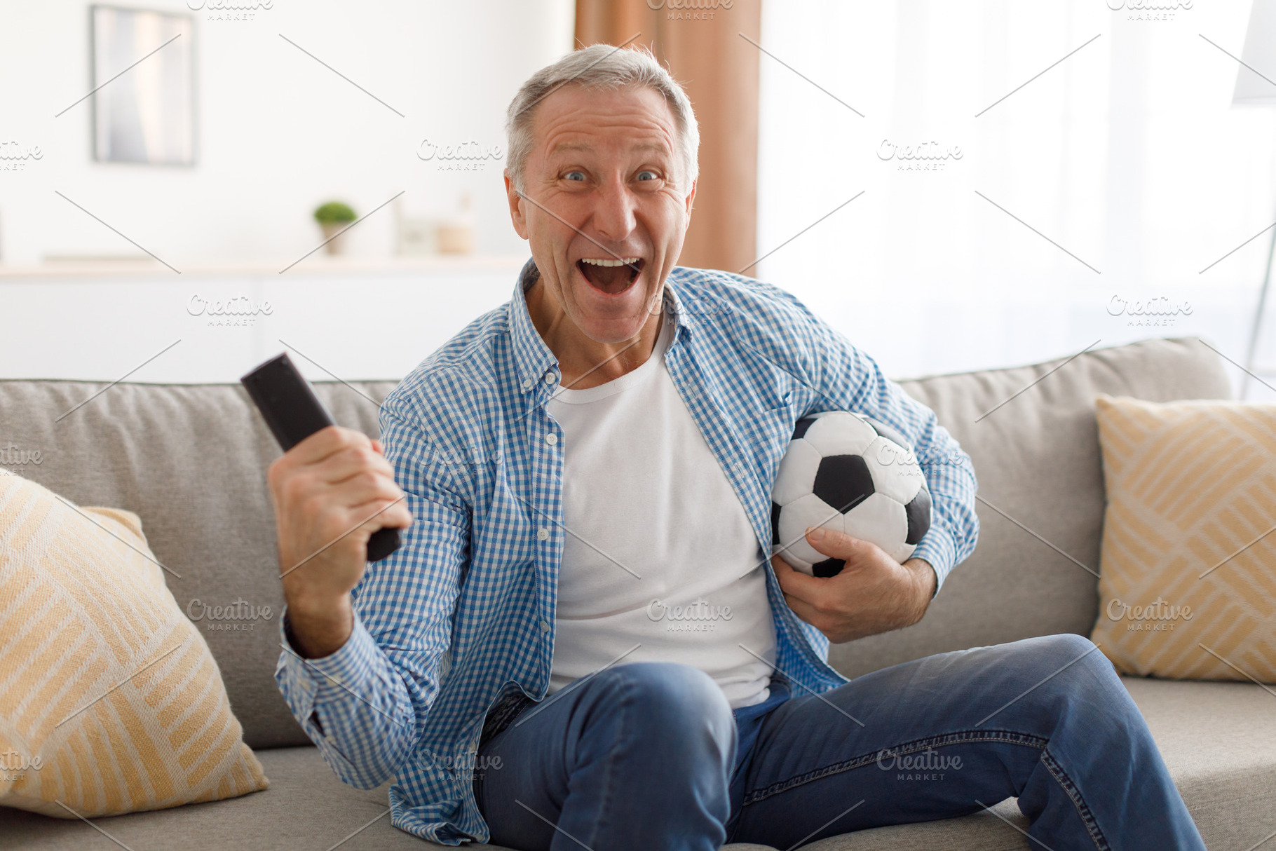 Excited mature man watching tv celebrating goal holding ball, a Photo by Prostock-Studio