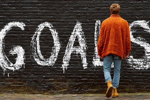 Person walking towards wall with word goals painted in white letters, a Photo by AS photostudio