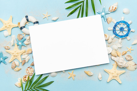 Blank card surrounded by seashells and starfish on sandy beach