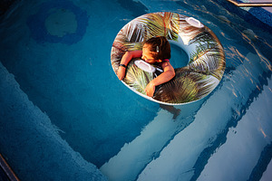 Child relaxing in a pool using an inflatable tube on a sunny day, a Photo by AS photostudio