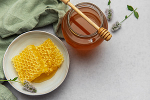 Honeycomb and honey jar with wooden dipper on marble table, a Food & Drink Photo by Olena Rudo