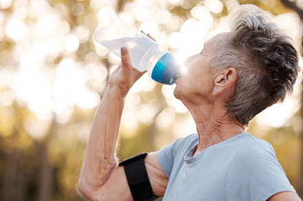 Senior woman runner, drinking water and workout in park, summer and training for health, cardio and fitness. Elderly running, exercise and hydration with water break for healthy body, mind or muscle, a Photo by Peopleimages.com