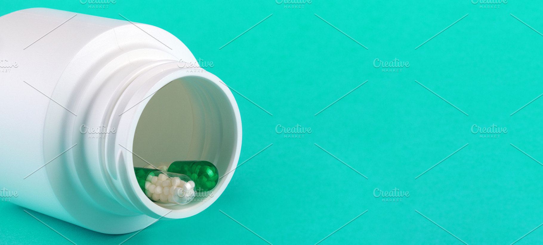 White pill bottle tipped over with green and white capsules on turquoise backgr, a Health & Medical Photo by Ales Munt