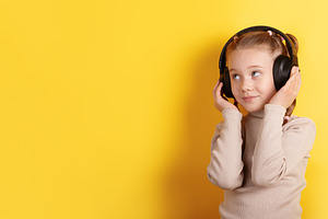 Smiling young girl wearing headphones against bright yellow back, a Person Photo by Ales Munt