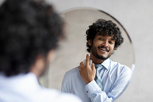Happy indian businessman in shirt and necktie spraying perfume on his neck whil, a Person Photo by Prostock-Studio