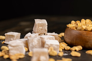 Turkish delight and toasted peanuts on a black slate surface, close up, a Photo by rsoollAI