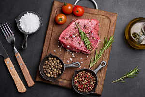 Fresh piece of raw beef on a wooden board with rosemary, cherry, a Food & Drink Photo by ndanko