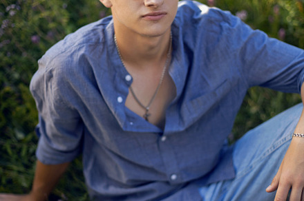 sexy teen guy in sunglasses is sitting on the grass in nature in a shirt and je, a Person Photo by SaulichPhoto
