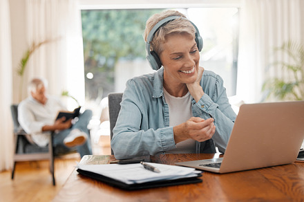 Remote woman, video call or laptop webinar training on online zoom call meeting in home office or house room interior. Smile, happy or elderly worker with headphones working on startup tech interview, a Photo by Peopleimages.com