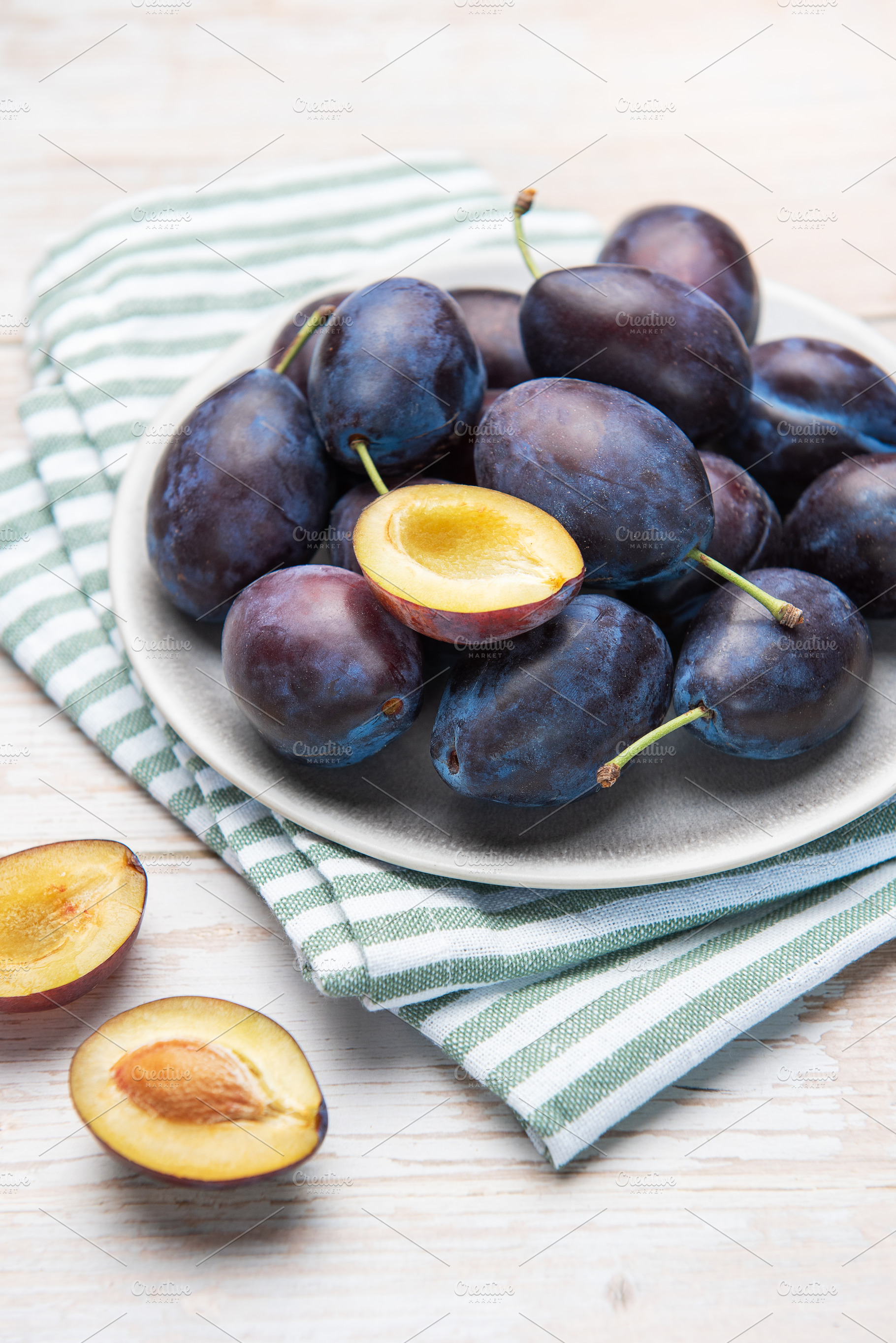 Fresh ripe plums in grey bowl on wood table, a Food & Drink Photo by Olena Rudo