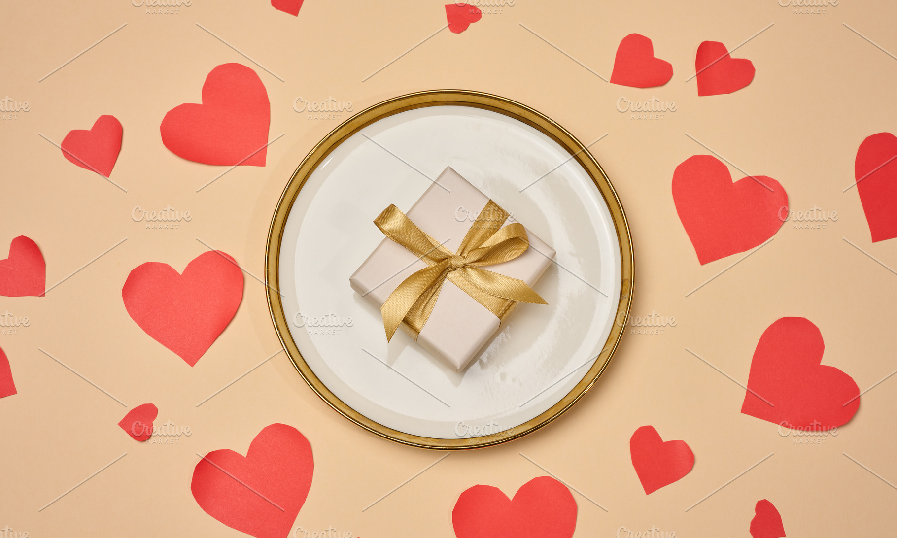 A gift with a gold bow on a plate surrounded by red hearts on a, a Holiday Photo by ndanko