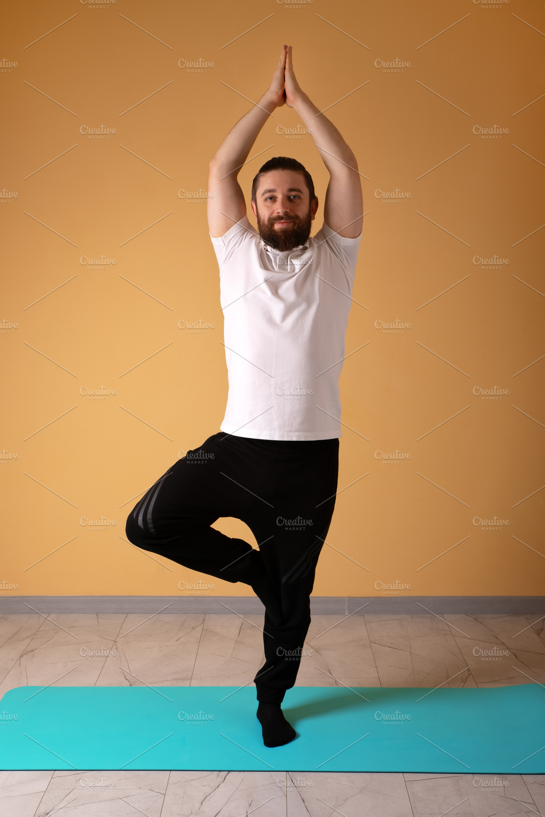 Adult male standing in tree pose on a turquoise mat indoors, aga, a Person Photo by Ales Munt