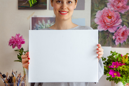 Smiling young woman artist is holding a blank white canvas
