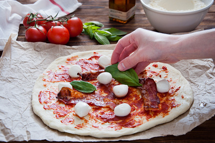 Cooking homemade pizza containing bacon, basil, and cheese