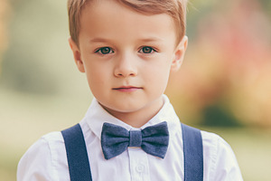 Young boy wearing a bow tie and suspenders, looking at camera wi, a Person Photo by Studio ANNA