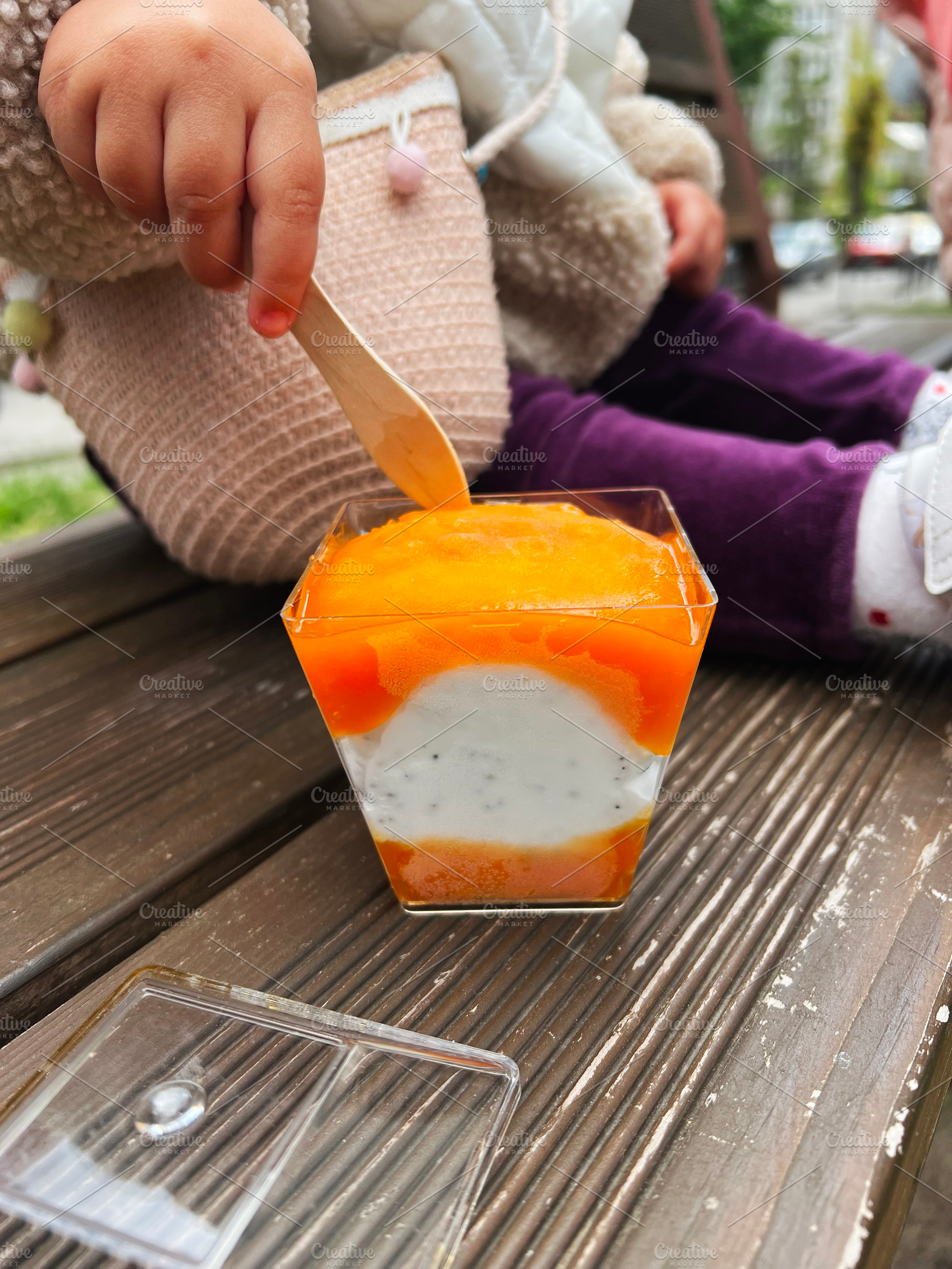 Child enjoying a delicious dessert on a wooden bench outdoors, a Photo by AS photostudio