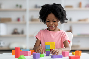 Smiling little african american girl playing with colorful wooden blocks, a Photo by Prostock-Studio