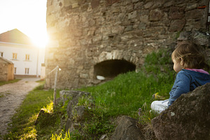Young child sitting near rustic stone building during a bright sunny day, a Person Photo by AS photostudio