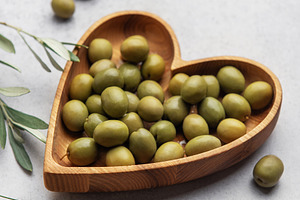 Fresh green olives displayed on wooden heart shaped bowl with ol, a Food & Drink Photo by Olena Rudo
