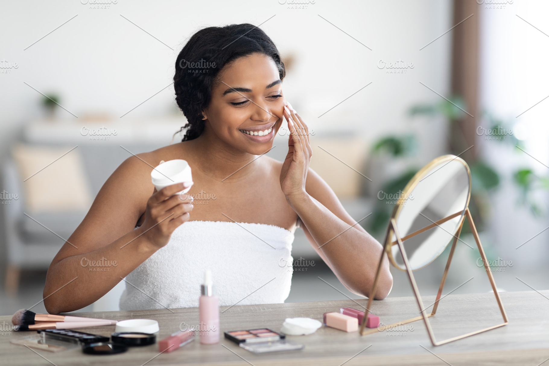 Cheerful attractive black woman using facial cream, a Photo by Prostock-Studio