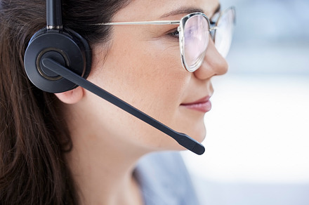 Closeup of one confident young caucasian call centre telemarketing agent wearing glasses and talking on headset while working in office. Face of female consultant operating helpdesk for customer service and sales support, a Photo by Peopleimages.com